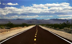 Looking down a straight road through desert to beautiful mountains and blue sky ahead symbolizes how straight, honest values help move us and our clients to a wonderful future.