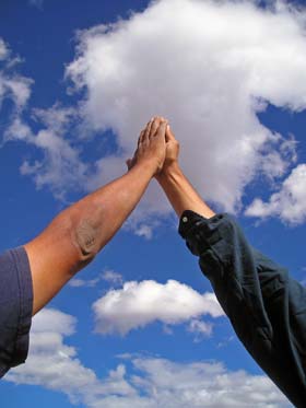 Two arms connect in a high five to celebrate success under cotton clouds and blue sky.