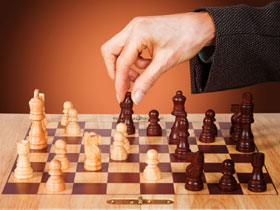 Hand moving a piece on a chess board.  Chess is a great symbol for the strategic work of deciding which markets to attack, with which resources, and how to apply them.